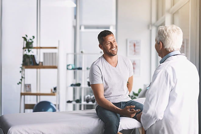 Young man with back pain talking to an orthopedic surgeon about spine care at Ascension sites of care. 