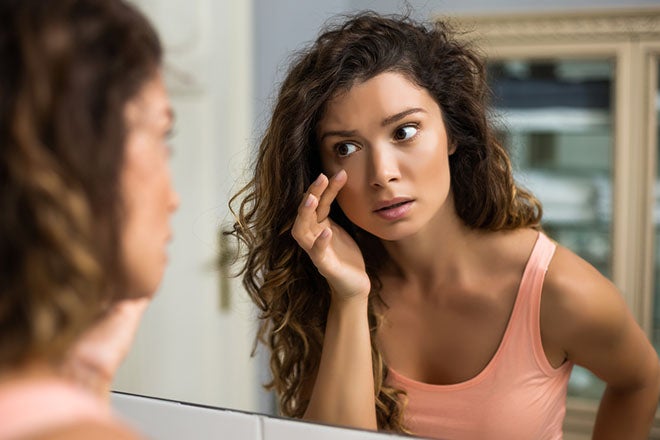 Woman looking at her skin in the mirror.