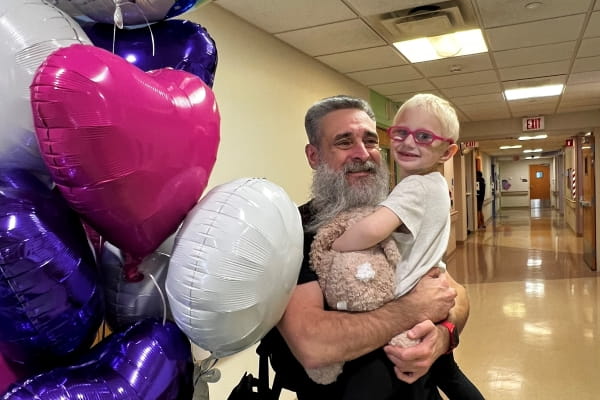 father holding daughter  at Peyton Manning Children's Hospital with pink, purple and white balloons next to them
