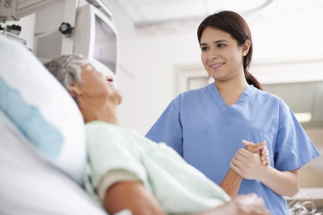 Woman in hospital bed with nurse holder her hand.