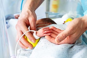 Father holding his infant child's hand in a hospital room.