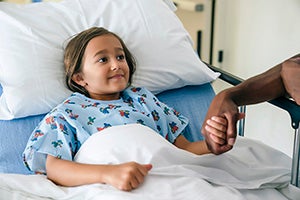 Dad holding his daughter's hand who is in a hospital bed.